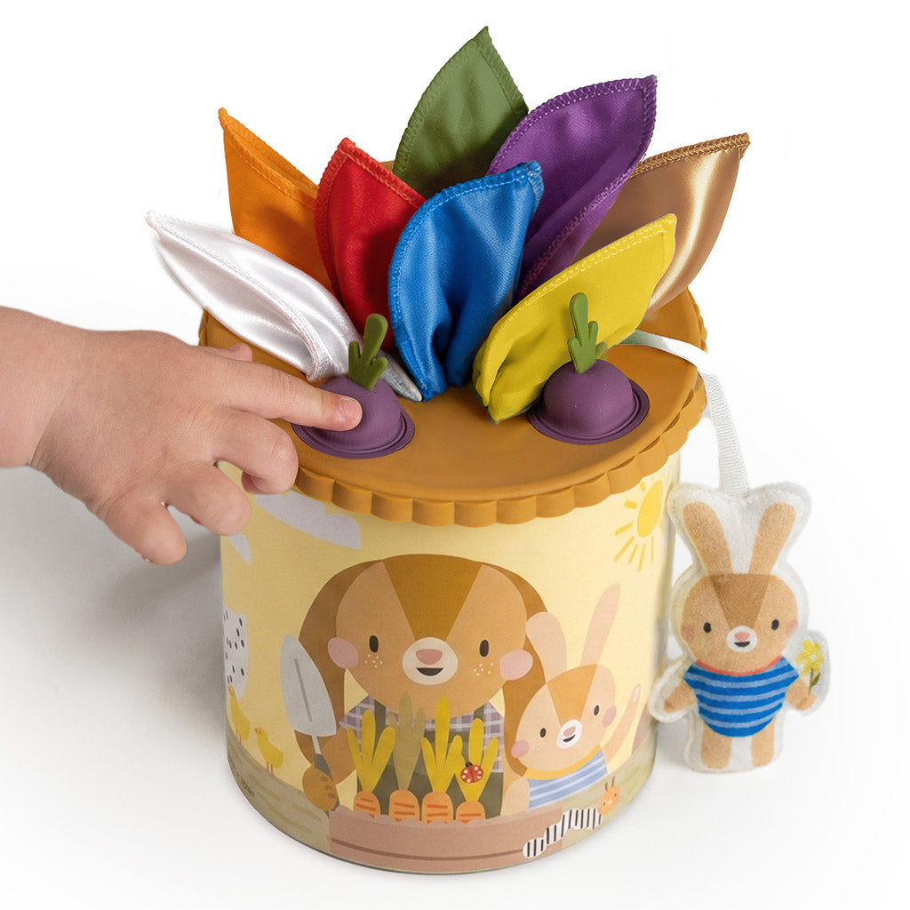 Taf Toys Pop & Pull Tissue Box showing colorful fabrics, beet silicone pop-its, and attached bunny doll