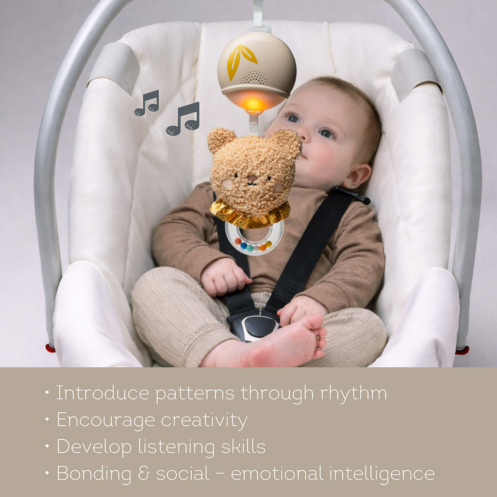 Infant looking up at the Taf Toys light up bear toy in a bassinet, highlighting benefits like rhythm patterns and listening skills
